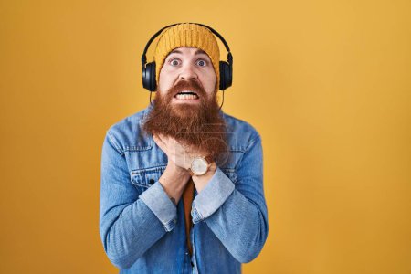 Photo for Caucasian man with long beard listening to music using headphones shouting suffocate because painful strangle. health problem. asphyxiate and suicide concept. - Royalty Free Image
