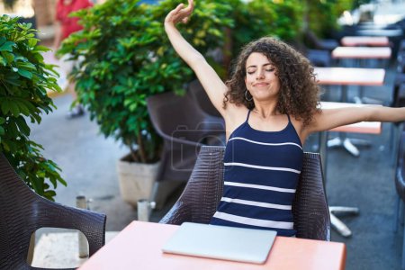 Téléchargez les photos : Jeune belle femme hispanique étirant les bras assis sur la table à la terrasse du café - en image libre de droit