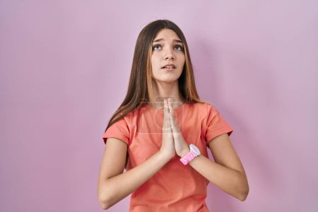 Téléchargez les photos : Teenager girl standing over pink background begging and praying with hands together with hope expression on face very emotional and worried. begging. - en image libre de droit