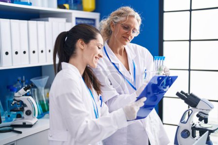 Téléchargez les photos : Deux femmes scientifiques écrivent sur un document contenant des éprouvettes en laboratoire - en image libre de droit