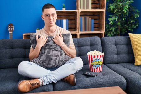 Photo for Young man eating popcorn clueless and confused expression. doubt concept. - Royalty Free Image