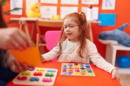 Téléchargez les photos : Adorable rousse fille jouer avec des mathématiques jeu de puzzle assis sur la table à la maternelle - en image libre de droit