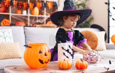 Foto de Adorable chica hispana con disfraz de halloween sosteniendo dulces en casa - Imagen libre de derechos