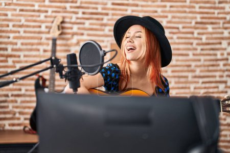 Foto de Young caucasian woman musician singing song playing classical guitar at music studio - Imagen libre de derechos
