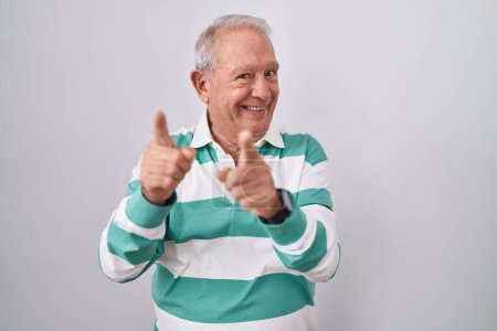Foto de Senior man with grey hair standing over white background pointing fingers to camera with happy and funny face. good energy and vibes. - Imagen libre de derechos