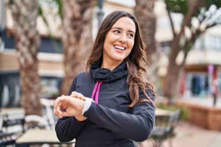 Téléchargez les photos : Jeune femme hispanique portant des vêtements de sport en utilisant chronomètre à la rue - en image libre de droit