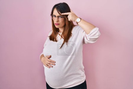 Photo for Pregnant woman standing over pink background pointing unhappy to pimple on forehead, ugly infection of blackhead. acne and skin problem - Royalty Free Image