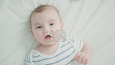 Téléchargez les photos : Adorable caucasian baby lying on bed with relaxed expression at bedroom - en image libre de droit
