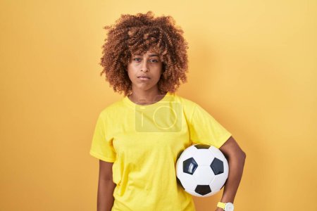 Photo for Young hispanic woman with curly hair holding football ball thinking attitude and sober expression looking self confident - Royalty Free Image