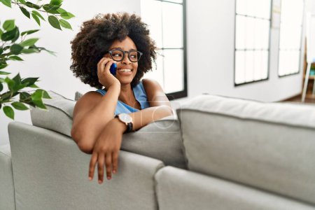 Téléchargez les photos : Jeune femme afro-américaine souriante confiante parler sur le smartphone à la maison - en image libre de droit