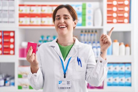 Téléchargez les photos : Brunette woman working at pharmacy drugstore holding condom smiling happy pointing with hand and finger to the side - en image libre de droit
