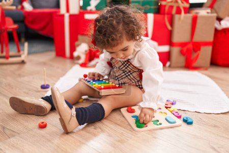 Foto de Adorable hispanic girl playing with maths game sitting on floor by christmas tree at home - Imagen libre de derechos