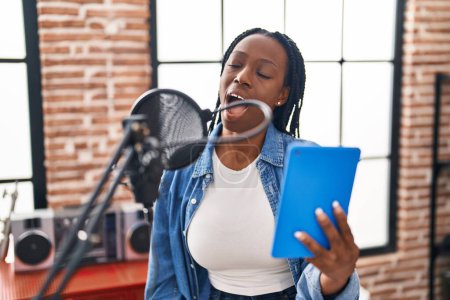 Téléchargez les photos : Artiste afro-américaine chantant une chanson tenant un pavé tactile au studio de musique - en image libre de droit
