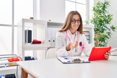 Photo for Young woman wearing doctor uniform using touchpad working at clinic - Royalty Free Image