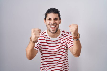Photo for Hispanic man with long hair standing over isolated background angry and mad raising fists frustrated and furious while shouting with anger. rage and aggressive concept. - Royalty Free Image