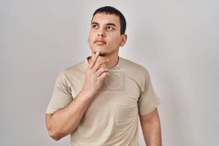 Foto de Hombre árabe joven con camiseta casual pensando concentrado en la duda con el dedo en la barbilla y mirando hacia arriba preguntándose - Imagen libre de derechos