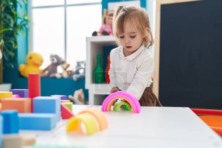 Téléchargez les photos : Adorable blonde girl playing with toys standing at kindergarten - en image libre de droit