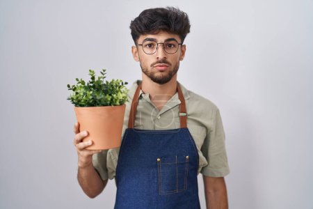 Téléchargez les photos : Arab man with beard holding green plant pot relaxed with serious expression on face. simple and natural looking at the camera. - en image libre de droit