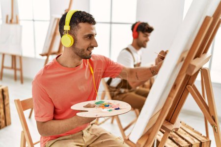 Foto de Dos hombres hispanos en pareja escuchando música y dibujando en el estudio de arte - Imagen libre de derechos