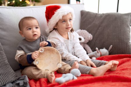 Téléchargez les photos : Frère et sœur jouant au tambourin assis sur le canapé près de l'arbre de Noël à la maison - en image libre de droit