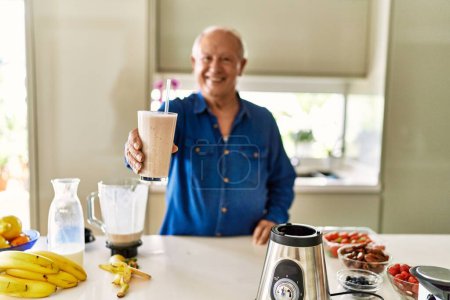 Foto de Hombre mayor sonriendo confiado sosteniendo el vaso de batido en la cocina - Imagen libre de derechos