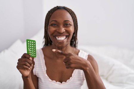 Photo for African american woman holding birth control pills smiling happy pointing with hand and finger - Royalty Free Image