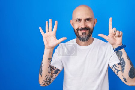 Photo for Hispanic man with tattoos standing over blue background showing and pointing up with fingers number seven while smiling confident and happy. - Royalty Free Image