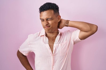 Téléchargez les photos : Jeune homme hispanique debout sur fond rose souffrant d'une blessure au cou, touchant le cou avec la main, douleur musculaire - en image libre de droit