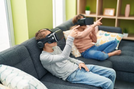 Téléchargez les photos : Deux enfants jouent à un jeu vidéo en utilisant des lunettes de réalité virtuelle à la maison - en image libre de droit