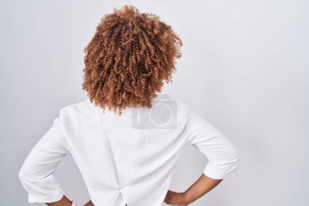 Photo for Young hispanic woman with curly hair standing over white background standing backwards looking away with arms on body - Royalty Free Image