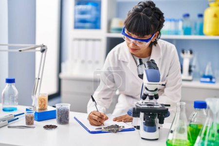 Téléchargez les photos : Young woman scientist writing on clipboard at laboratory - en image libre de droit