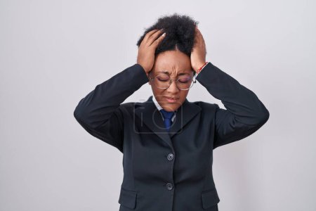 Foto de Beautiful african woman with curly hair wearing business jacket and glasses suffering from headache desperate and stressed because pain and migraine. hands on head. - Imagen libre de derechos