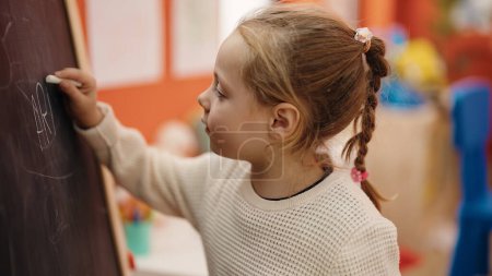 Photo for Adorable blonde girl preschool student drawing on blackboard at kindergarten - Royalty Free Image