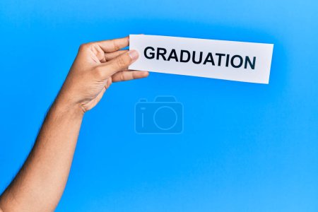 Téléchargez les photos : Hand of caucasian man holding paper with graduation word over isolated blue background - en image libre de droit