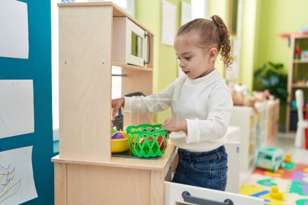Téléchargez les photos : Adorable blonde girl playing with play kitchen standing at kindergarten - en image libre de droit