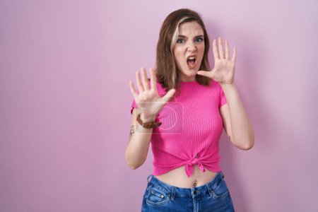 Photo for Blonde caucasian woman standing over pink background afraid and terrified with fear expression stop gesture with hands, shouting in shock. panic concept. - Royalty Free Image