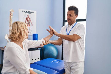 Photo for Middle age man and woman physiotherapist and patient stretching arm having rehab session at physiotherapy clinic - Royalty Free Image