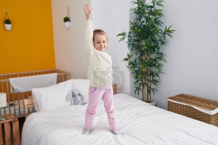Foto de Adorable chica rubia de pie en la cama con las manos levantadas en el dormitorio - Imagen libre de derechos