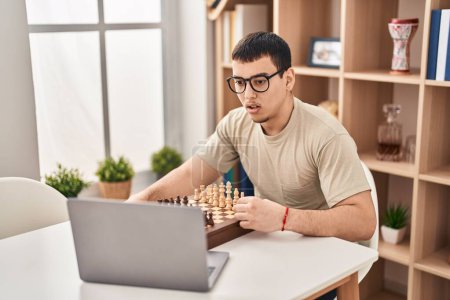 Téléchargez les photos : Jeune homme arabe jouant aux échecs en ligne effrayé et étonné avec la bouche ouverte pour la surprise, visage incrédule - en image libre de droit