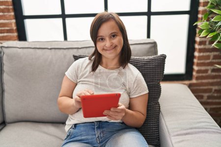 Foto de Síndrome de Down mujer usando touchpad sentado en el sofá en casa - Imagen libre de derechos