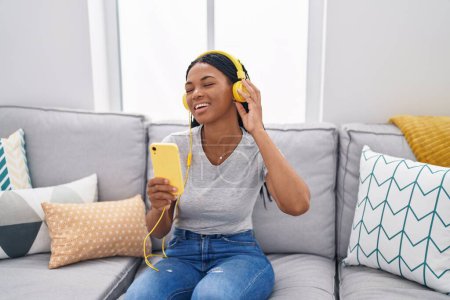 Téléchargez les photos : Femme afro-américaine écoutant de la musique assise sur le canapé à la maison - en image libre de droit