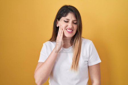 Téléchargez les photos : Young brunette woman standing over yellow background touching mouth with hand with painful expression because of toothache or dental illness on teeth. dentist - en image libre de droit