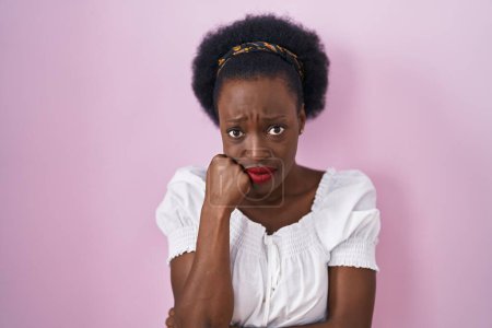 Photo for African woman with curly hair standing over pink background looking stressed and nervous with hands on mouth biting nails. anxiety problem. - Royalty Free Image