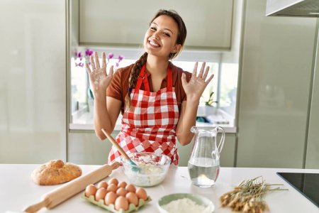 Foto de Young beautiful hispanic woman smiling confident showing hands with flour at the kitchen - Imagen libre de derechos