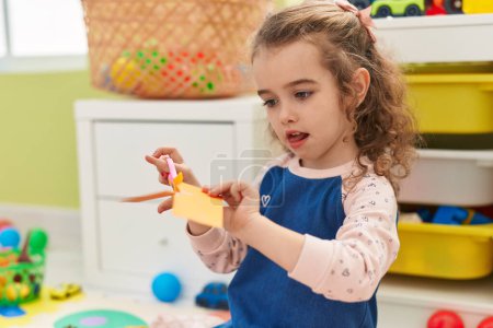Photo for Adorable blonde girl student cutting paper sitting on floor at kindergarten - Royalty Free Image