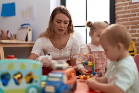 Photo for Teacher with boy and girl playing with toys sitting on table at kindergarten - Royalty Free Image