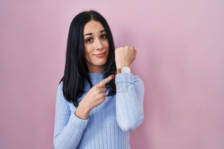Photo for Hispanic woman standing over pink background in hurry pointing to watch time, impatience, looking at the camera with relaxed expression - Royalty Free Image