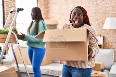 Foto de Dos mujeres africanas se mudan a un nuevo hogar celebrando locos y sorprendidos por el éxito con los ojos abiertos gritando emocionados. - Imagen libre de derechos