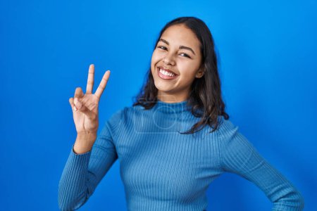 Photo for Young brazilian woman standing over blue isolated background smiling looking to the camera showing fingers doing victory sign. number two. - Royalty Free Image