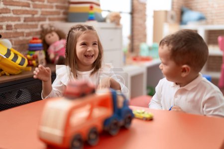 Foto de Adorable chica y niño jugando con coches en la mesa en el jardín de infantes - Imagen libre de derechos